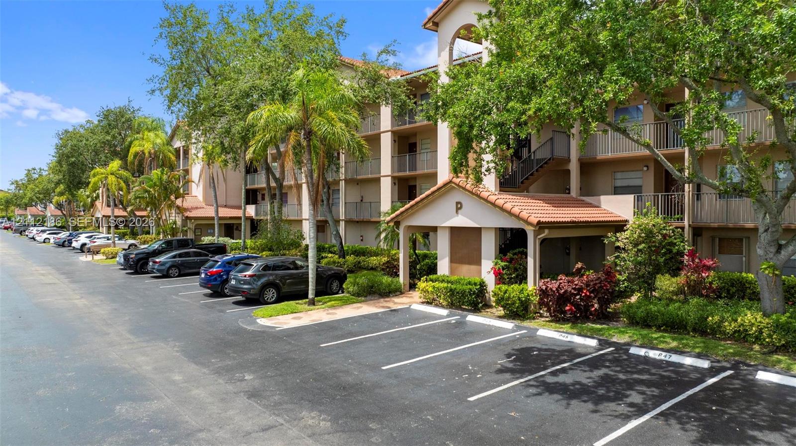 Multi-story residential building featuring a tile roof, private balcony access, covered parking entry, and established landscaping