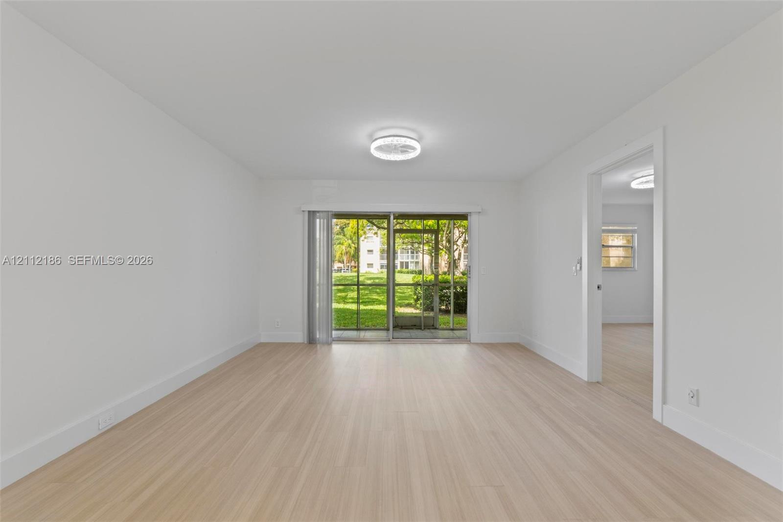 Open-concept room featuring light-toned wood-finish flooring, a contemporary flush-mount ceiling fixture, and a sliding glass door providing access to a screened outdoor area