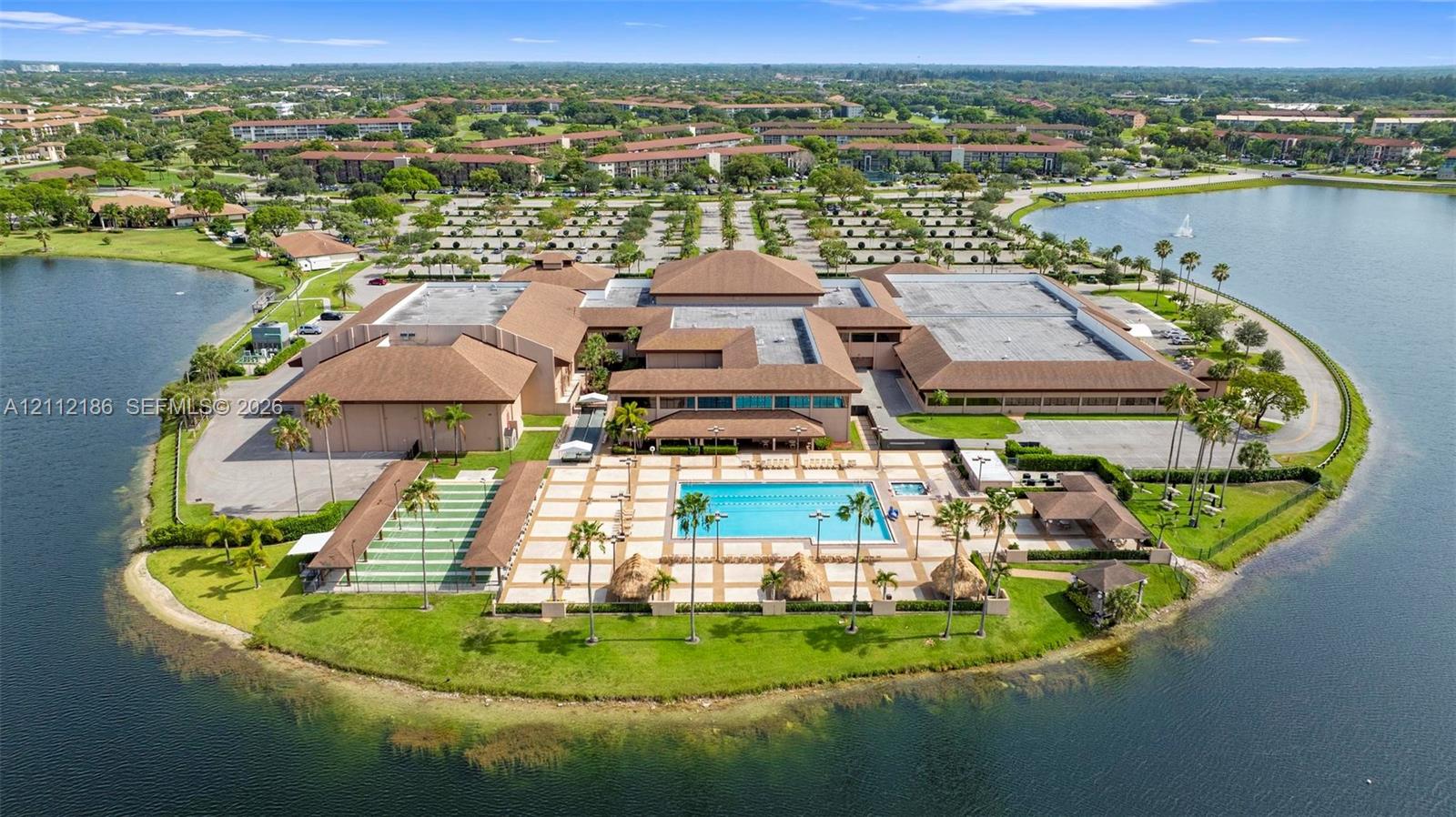 Waterfront property featuring a paved pool deck, swimming pool, shuffleboard court, and mature palm trees