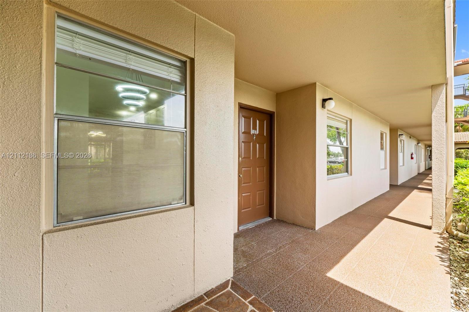 Covered walkway featuring a paneled entry door, dual-pane windows, and textured exterior finish