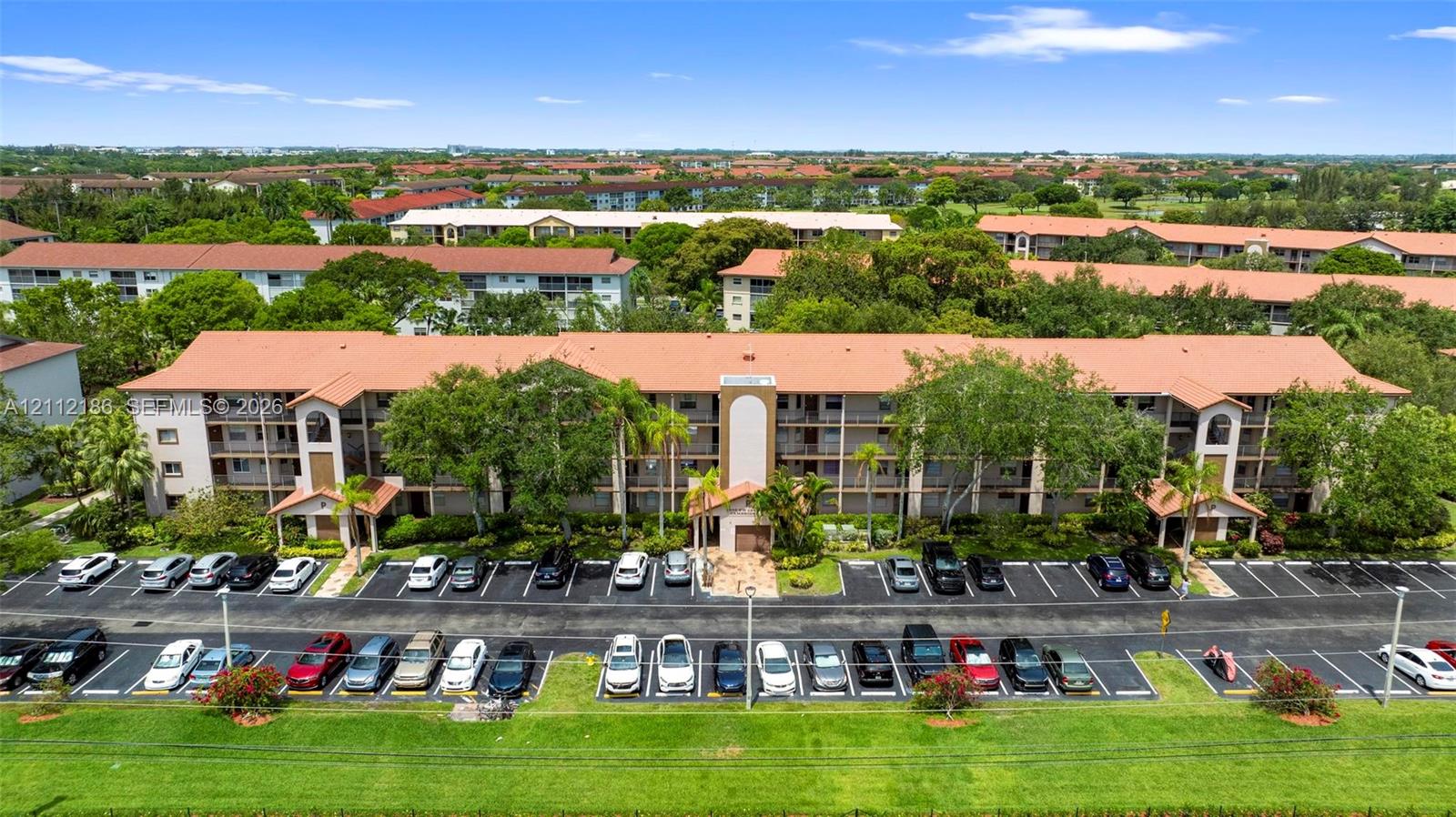 Multi-story residential building featuring a terracotta-tiled roof, covered breezeways, exterior balconies, and paved surface parking
