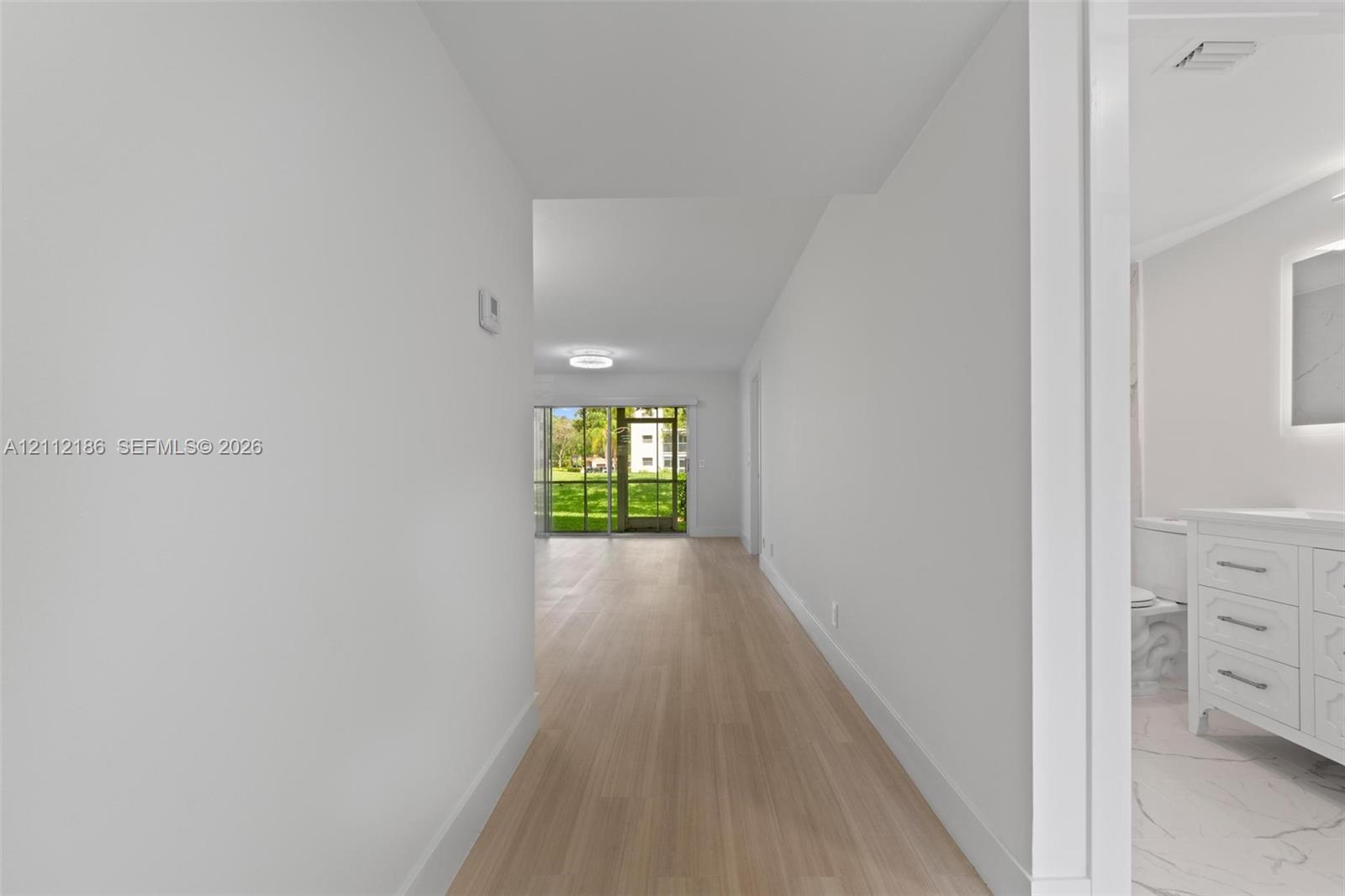 Interior hallway featuring light-toned wood-finish flooring and a bathroom vanity with a lighted mirror