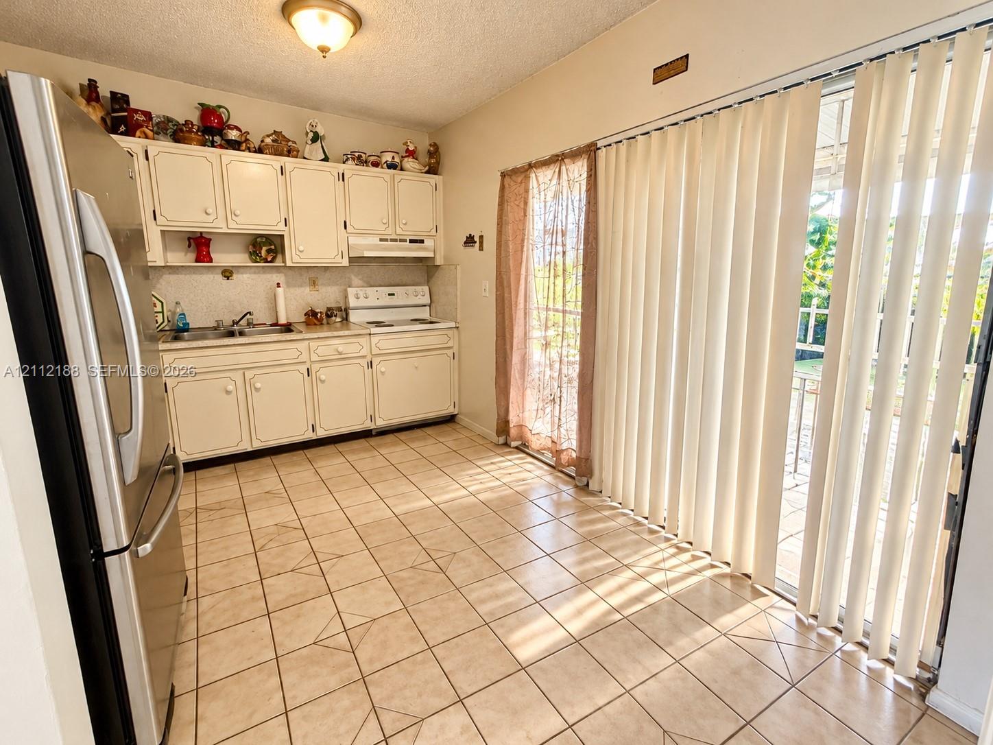 Kitchen featuring white cabinetry, stainless steel refrigerator, white electric range, tile flooring, and floor-to-ceiling sliding glass doors