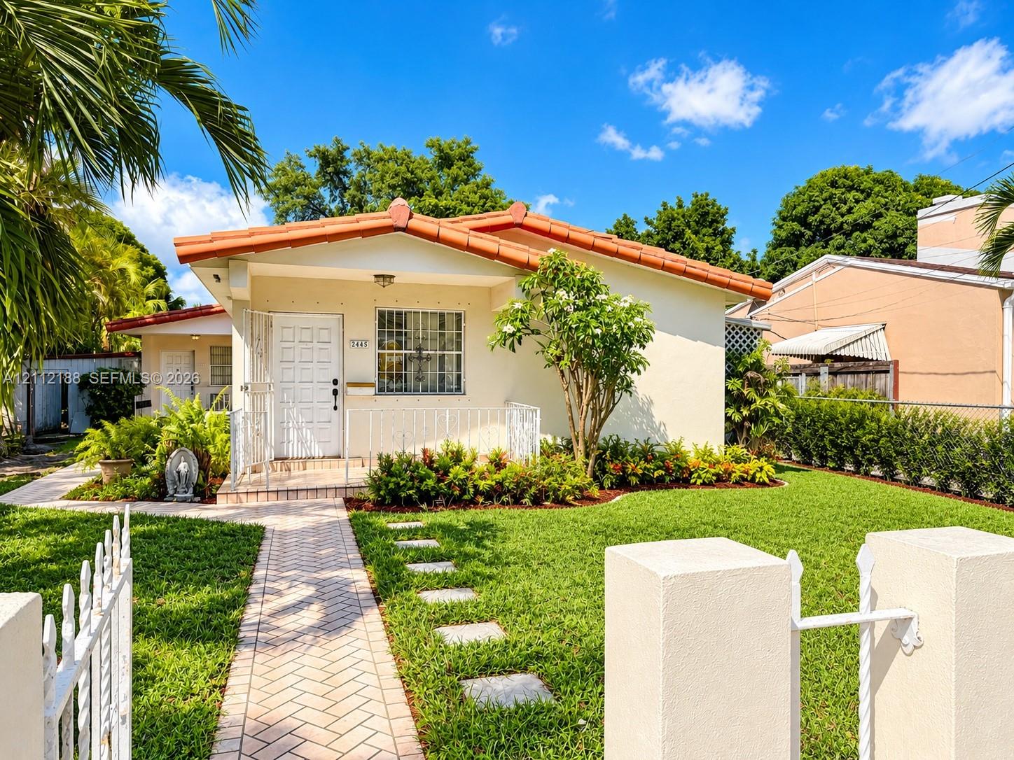Single-story residence featuring a tile roof, stucco exterior, covered front porch with white metal railings, and a brick-patterned paved walkway