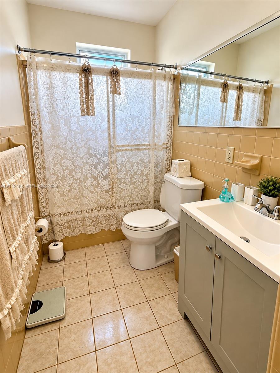 Bathroom featuring square tile flooring, wall-mounted mirror, vanity cabinet with integrated sink, and tile-surround shower area