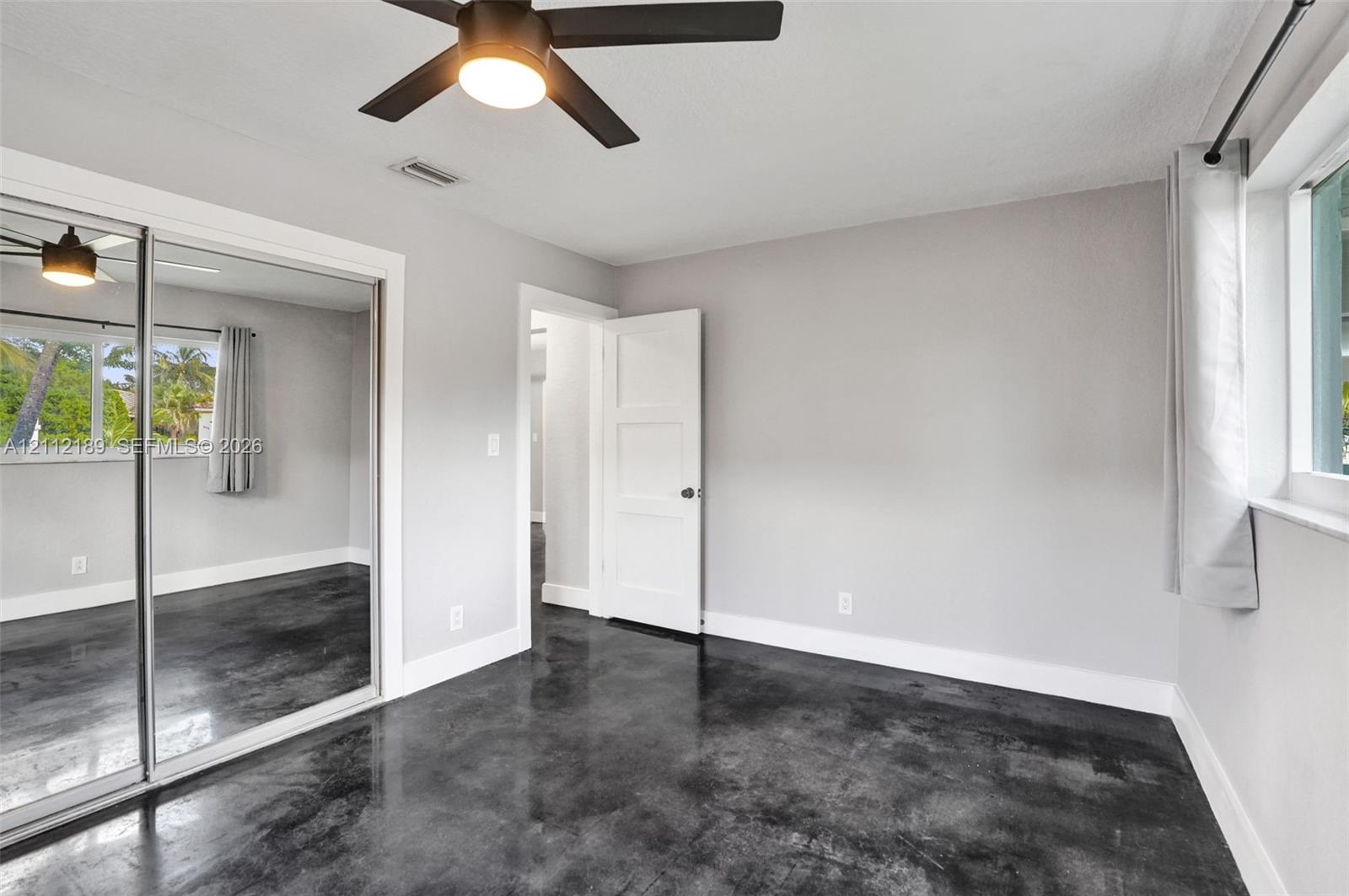 Polished concrete flooring, floor-to-ceiling mirrored sliding closet doors, and a modern ceiling fan with integrated lighting