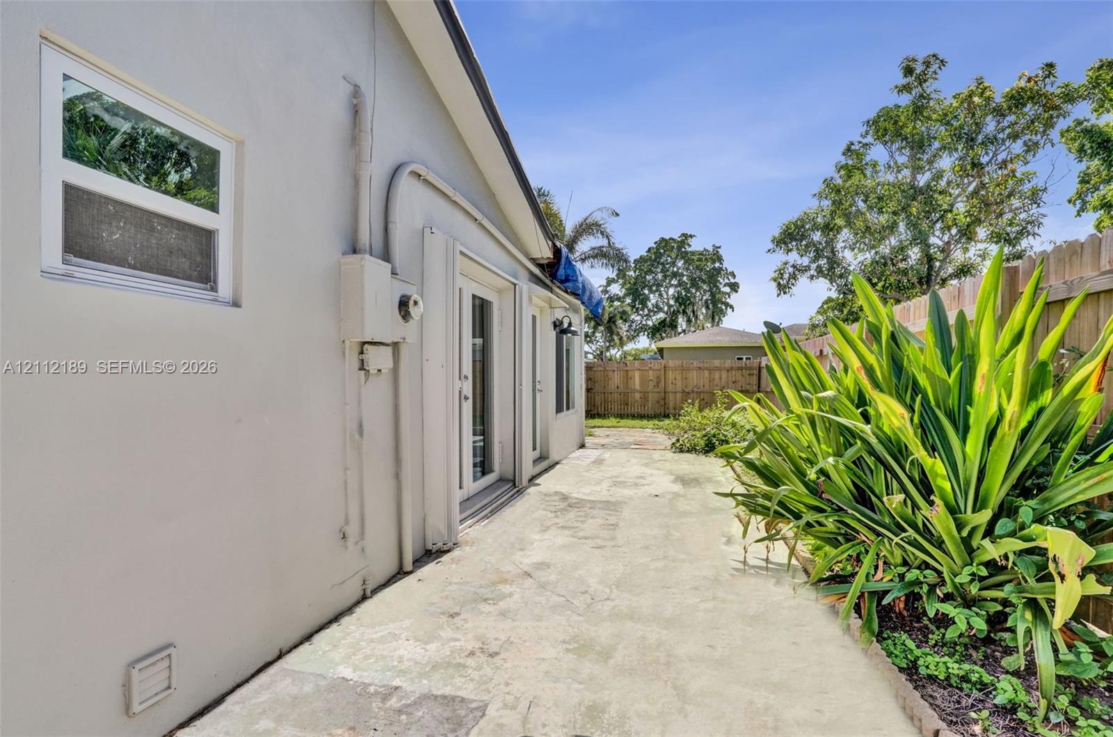 Concrete patio featuring dual glass-panel exterior doors, stucco siding, and a wooden privacy fence