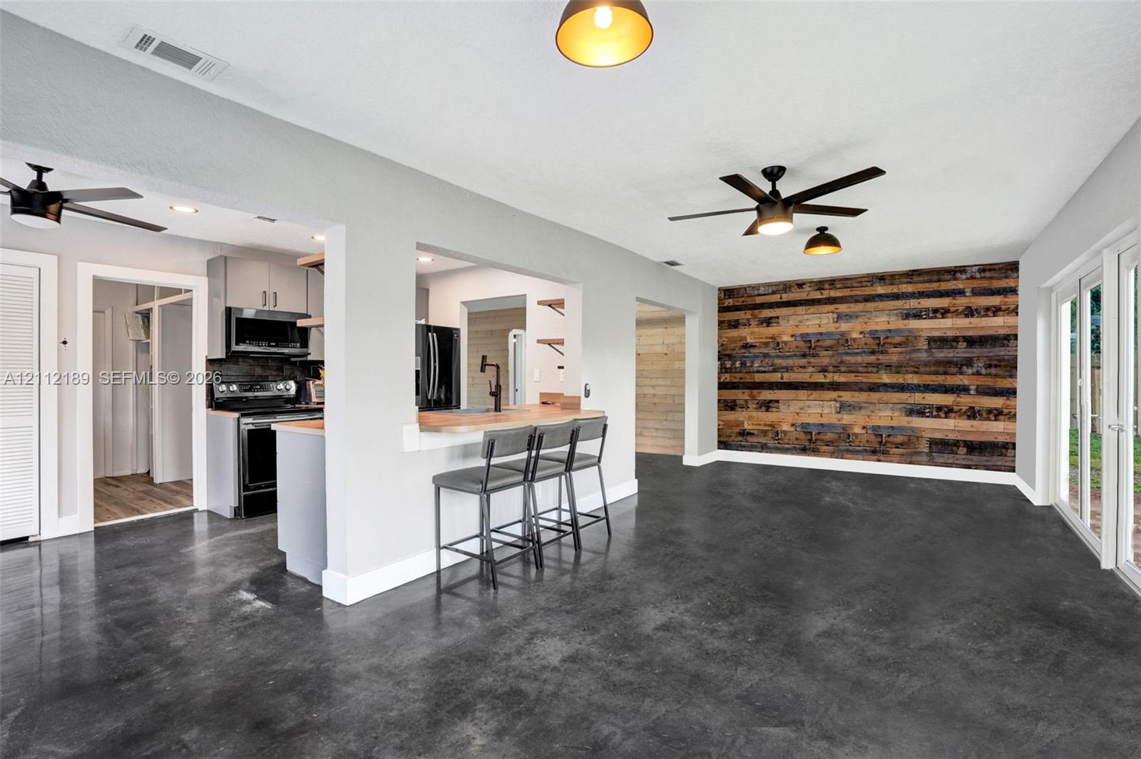 Open concept living area featuring dark polished concrete flooring, a horizontal reclaimed wood-plank accent wall, ceiling fans, and glass sliding doors