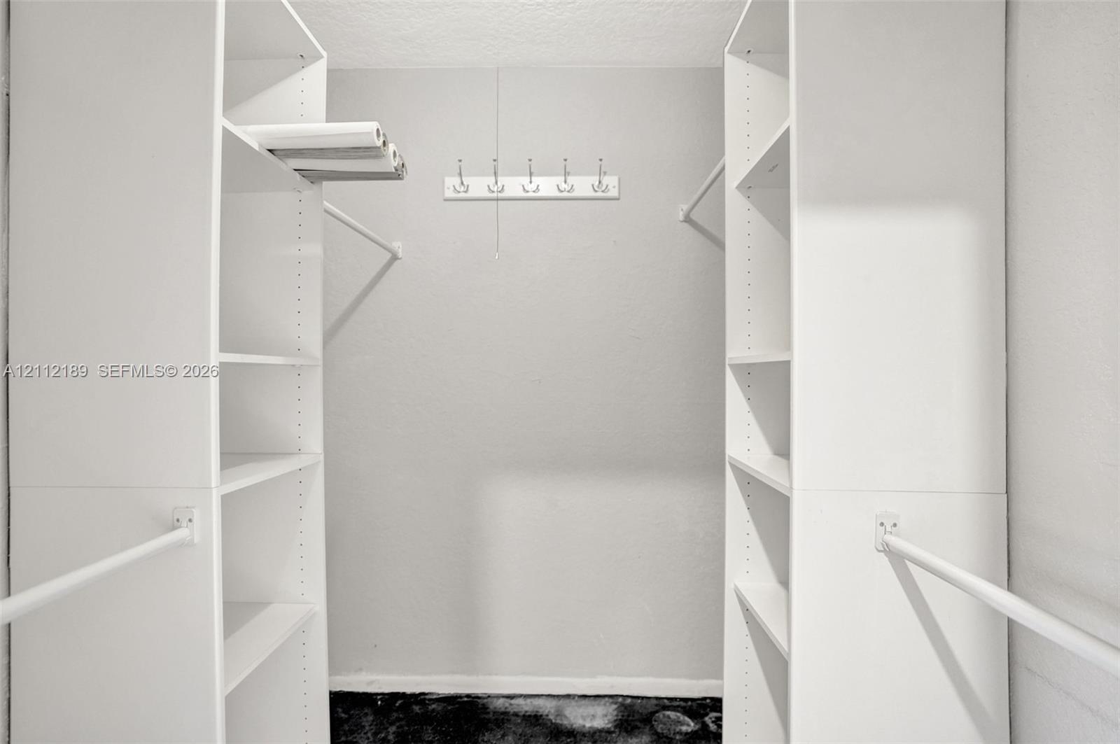 Walk-in closet featuring dual floor-to-ceiling built-in white shelving units, horizontal hanging rods, and a wall-mounted hook rack
