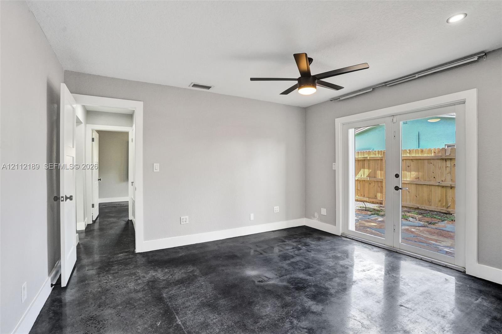 Polished concrete flooring, recessed lighting, matte black ceiling fan, and double glass doors featuring white trim