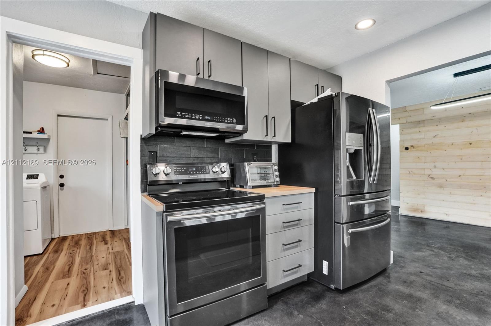 Kitchen featuring gray slab-front cabinetry, stainless steel appliances, a dark stone-finish backsplash, wood-surface countertops, and recessed lighting