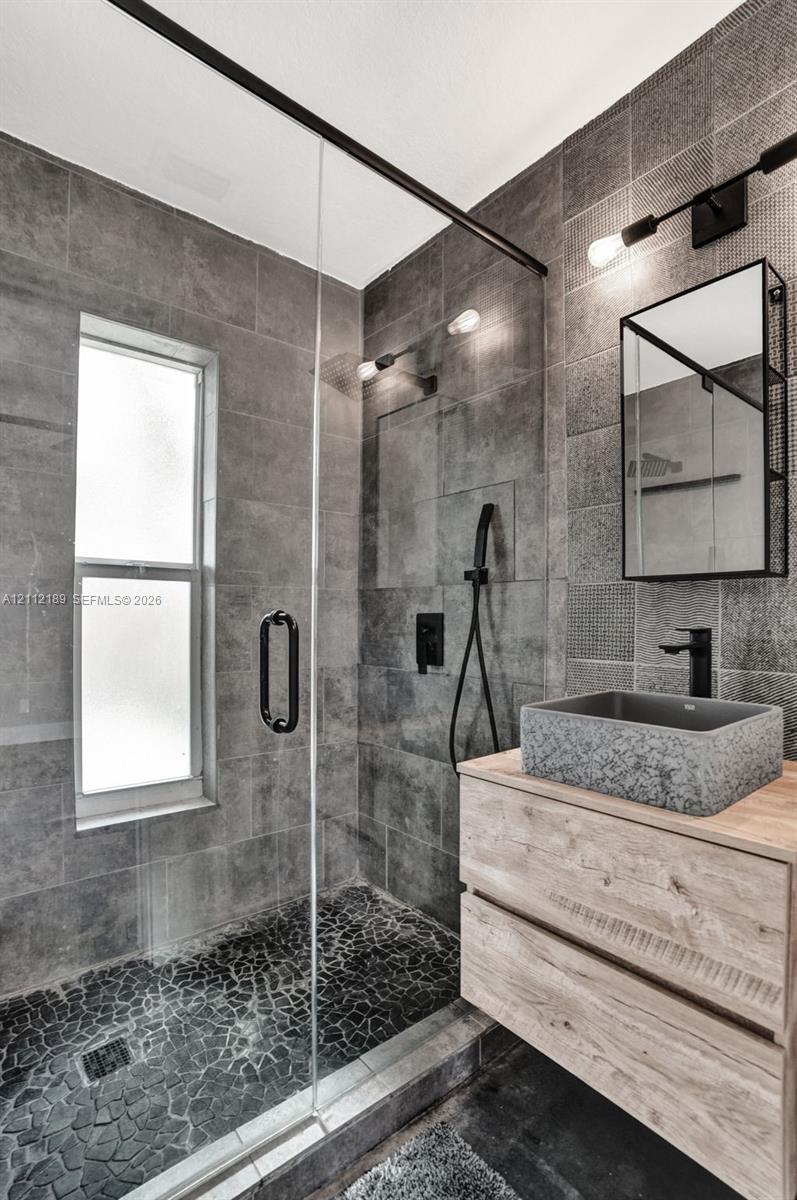 Walk-in shower featuring glass paneling, floor-to-ceiling gray tile, and a pebble-stone basin