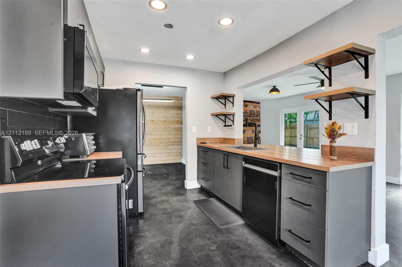 Kitchen featuring flat-panel charcoal cabinetry, wood-tone countertops, matte black hardware, recessed ceiling lighting, and open wall-mounted shelving