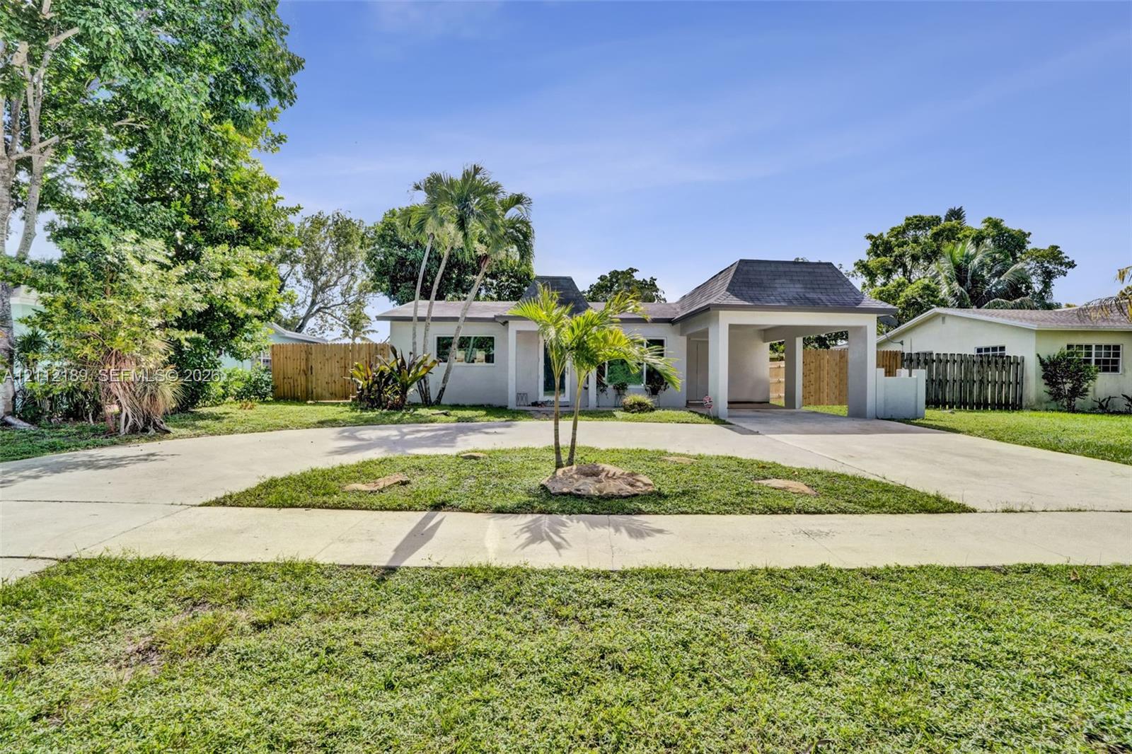 Single-story exterior featuring a hip roof, a concrete circular driveway, an attached carport, and mature palm trees