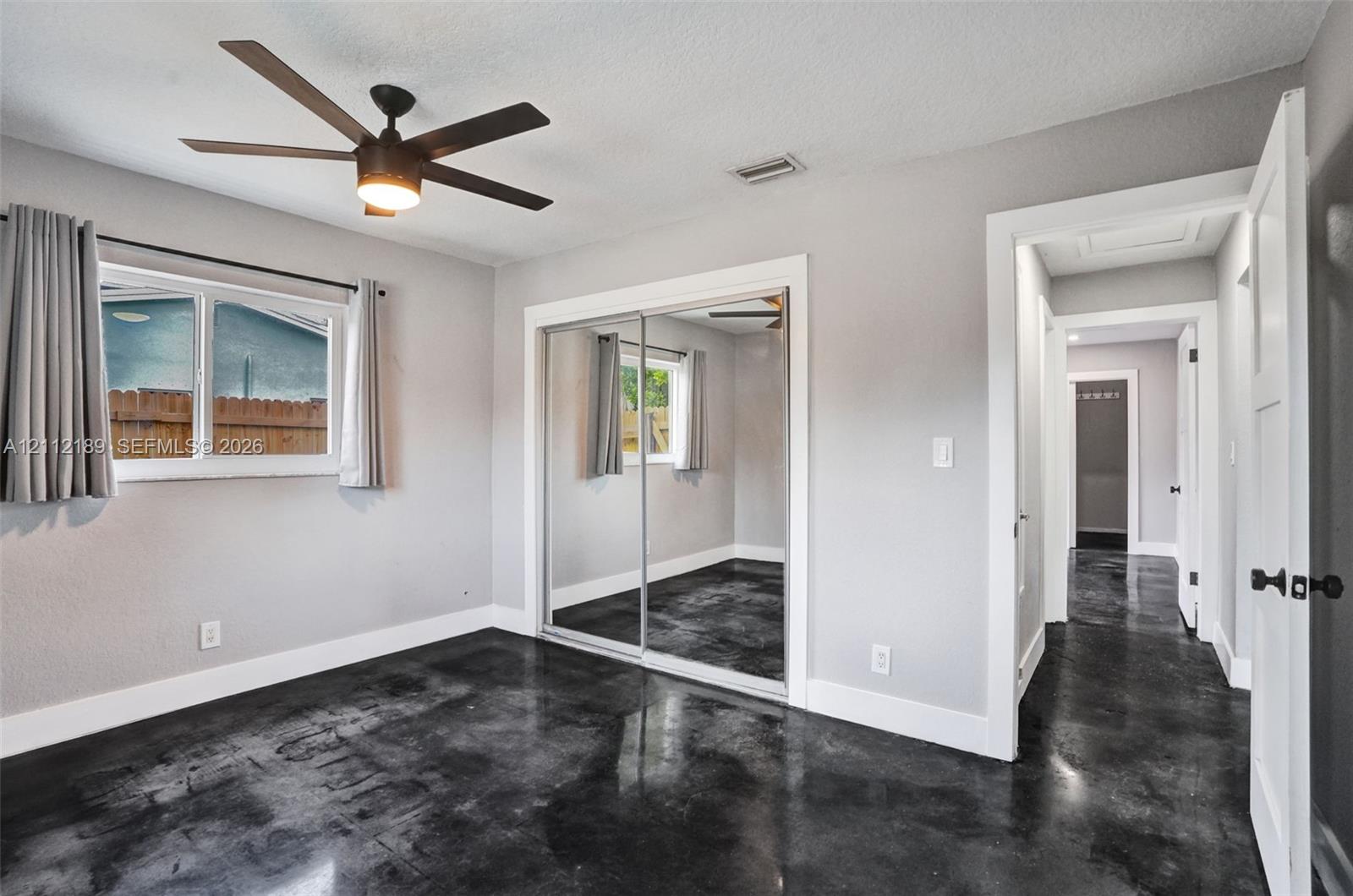 Polished concrete flooring, ceiling fan with integrated lighting, and mirrored sliding closet doors