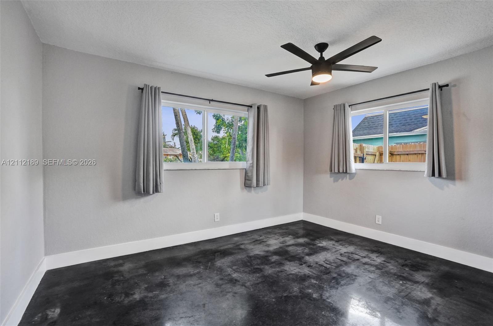 Interior space featuring stained concrete flooring, neutral wall tones, sliding windows, and a matte black ceiling fan