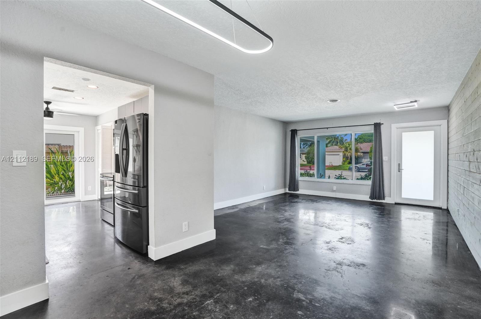 Polished concrete flooring, linear pendant lighting, built-in stainless steel refrigerator, textured wood-plank accent wall, and large picture window