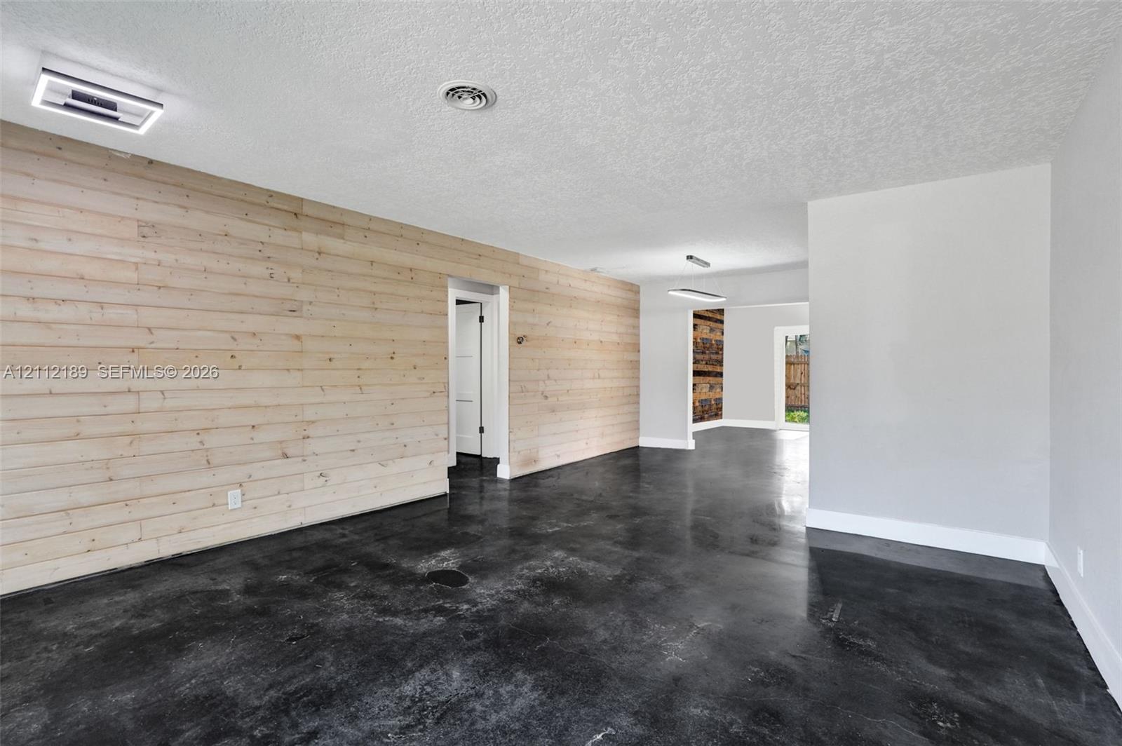 Interior space featuring horizontal light wood-plank wall paneling, polished concrete flooring, flush-mount LED lighting, and textured ceilings