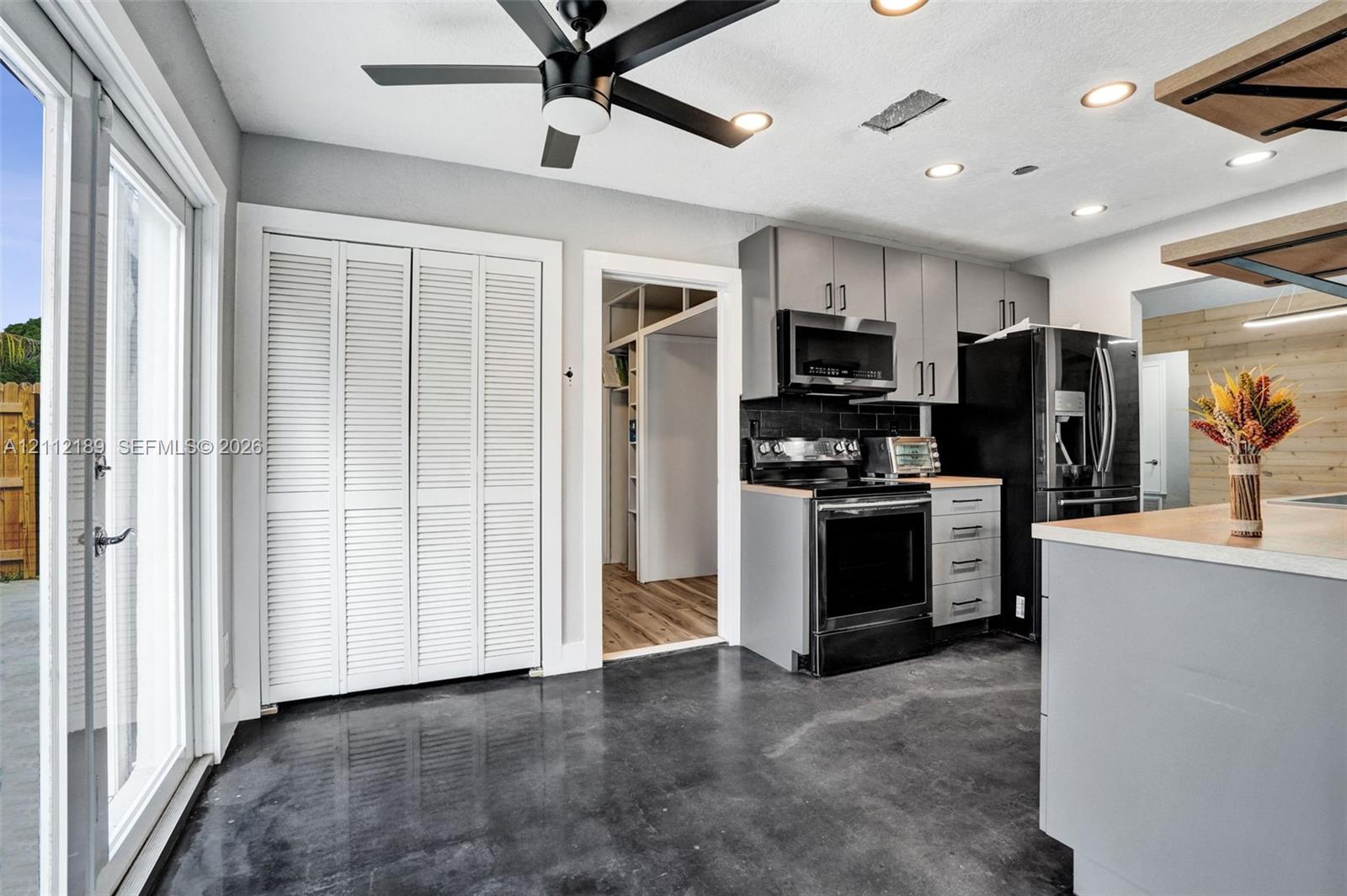 Kitchen featuring charcoal-toned cabinetry, stainless steel appliances, polished concrete flooring, a ceiling fan, and double glass patio doors