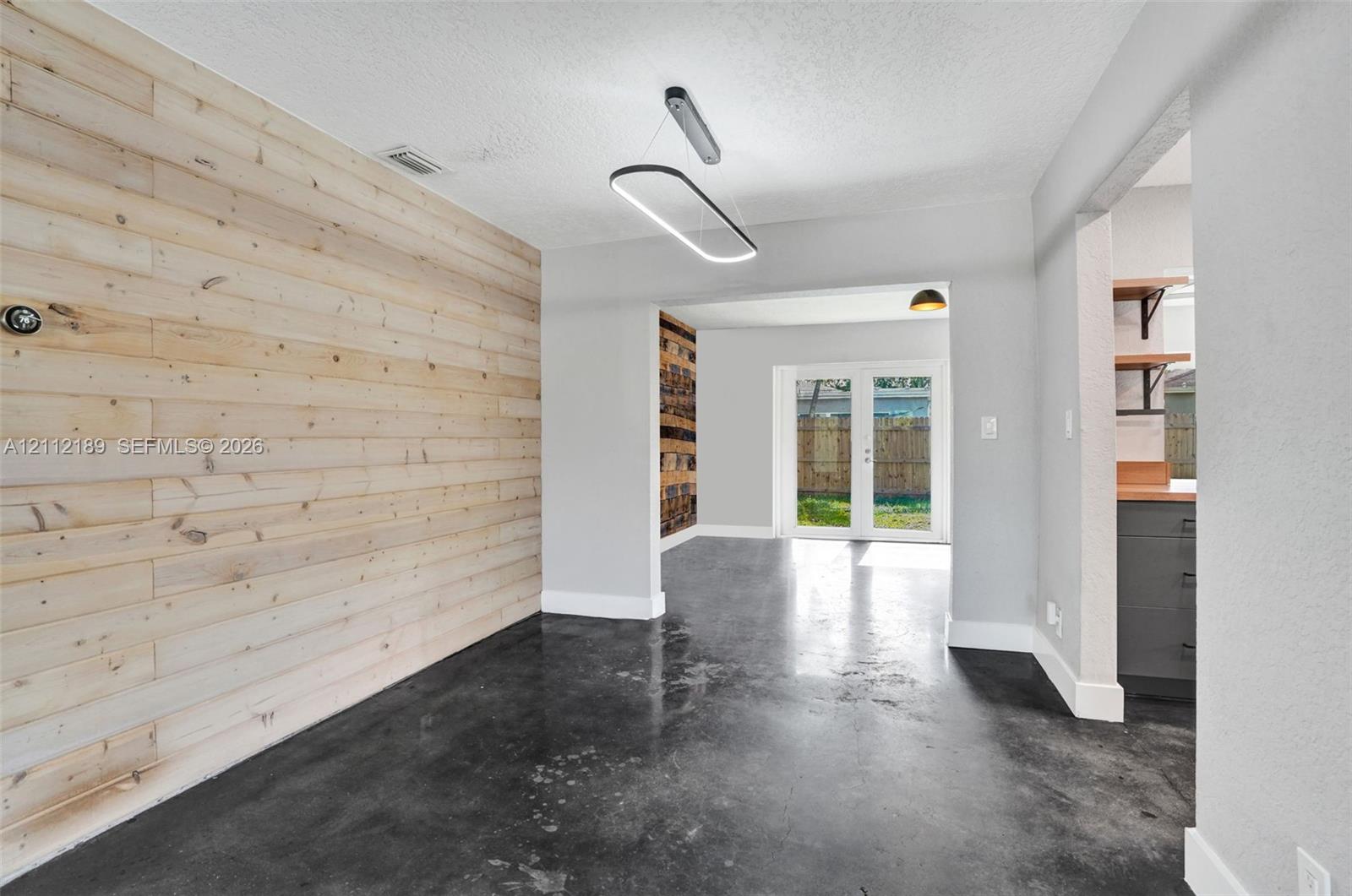 Interior space featuring horizontal natural wood-finish wall paneling, polished concrete flooring, a contemporary oval LED light fixture, and double glass-paned doors