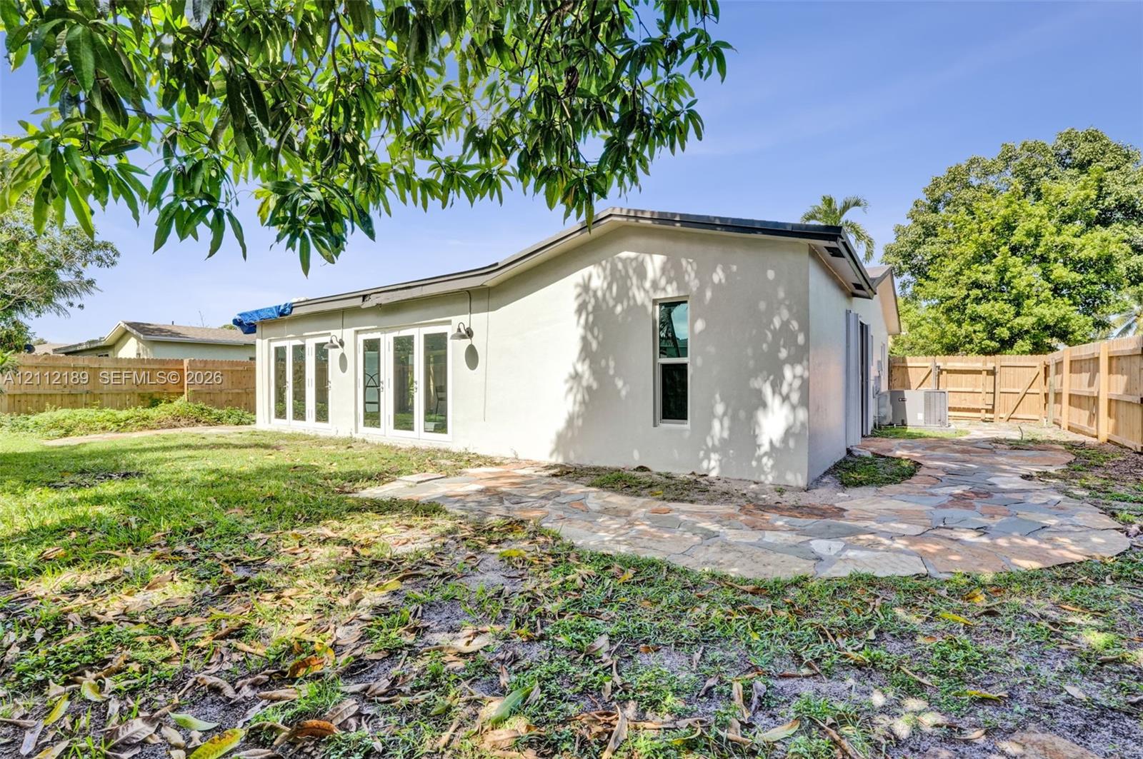 Stucco exterior featuring multiple sets of white-framed glass doors, a flagstone patio, and wood-panel fencing