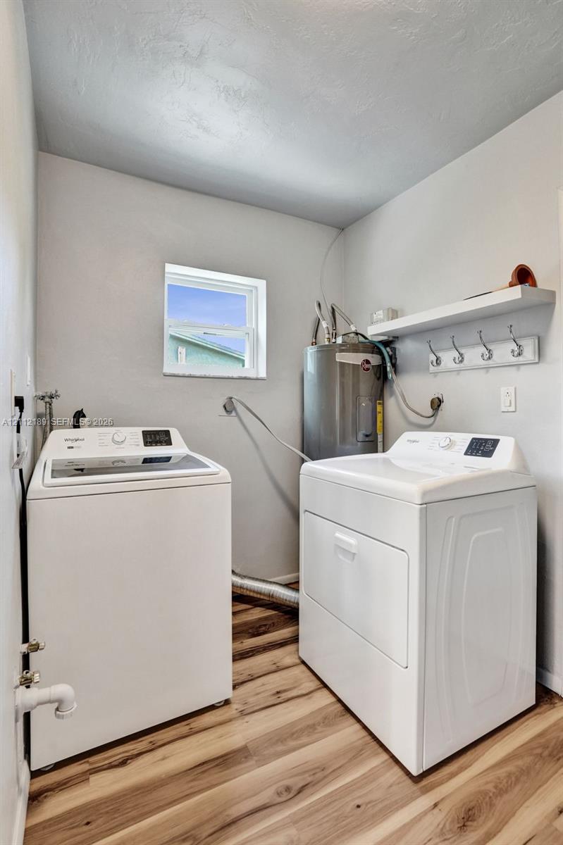 Laundry area featuring wood-finish flooring, a built-in wall shelf with a row of coat hooks, and a dedicated water heater