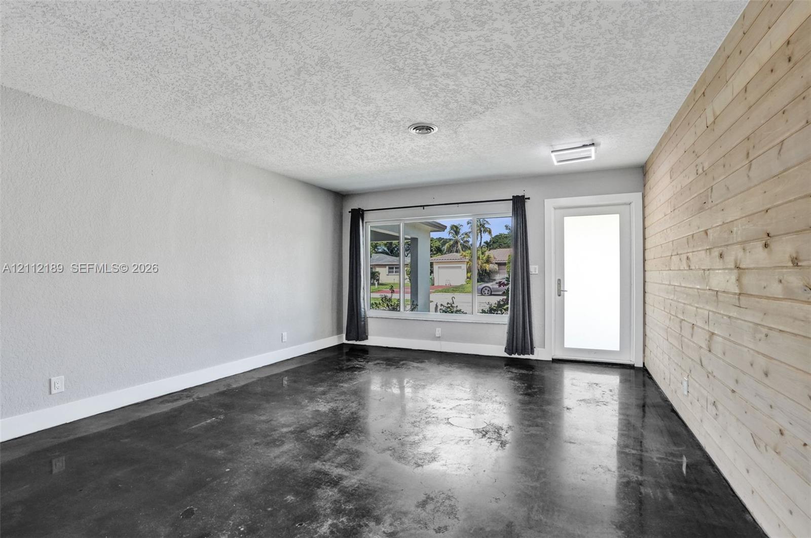 Polished concrete flooring, horizontal wood-plank accent wall, large picture window, and exterior door with frosted glass insert