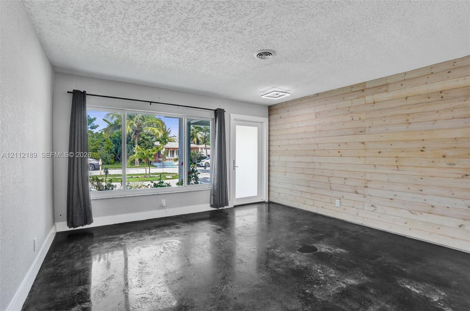 Interior space featuring a horizontal wood-plank accent wall, polished concrete flooring, large multi-pane window, and glass-paneled exterior door