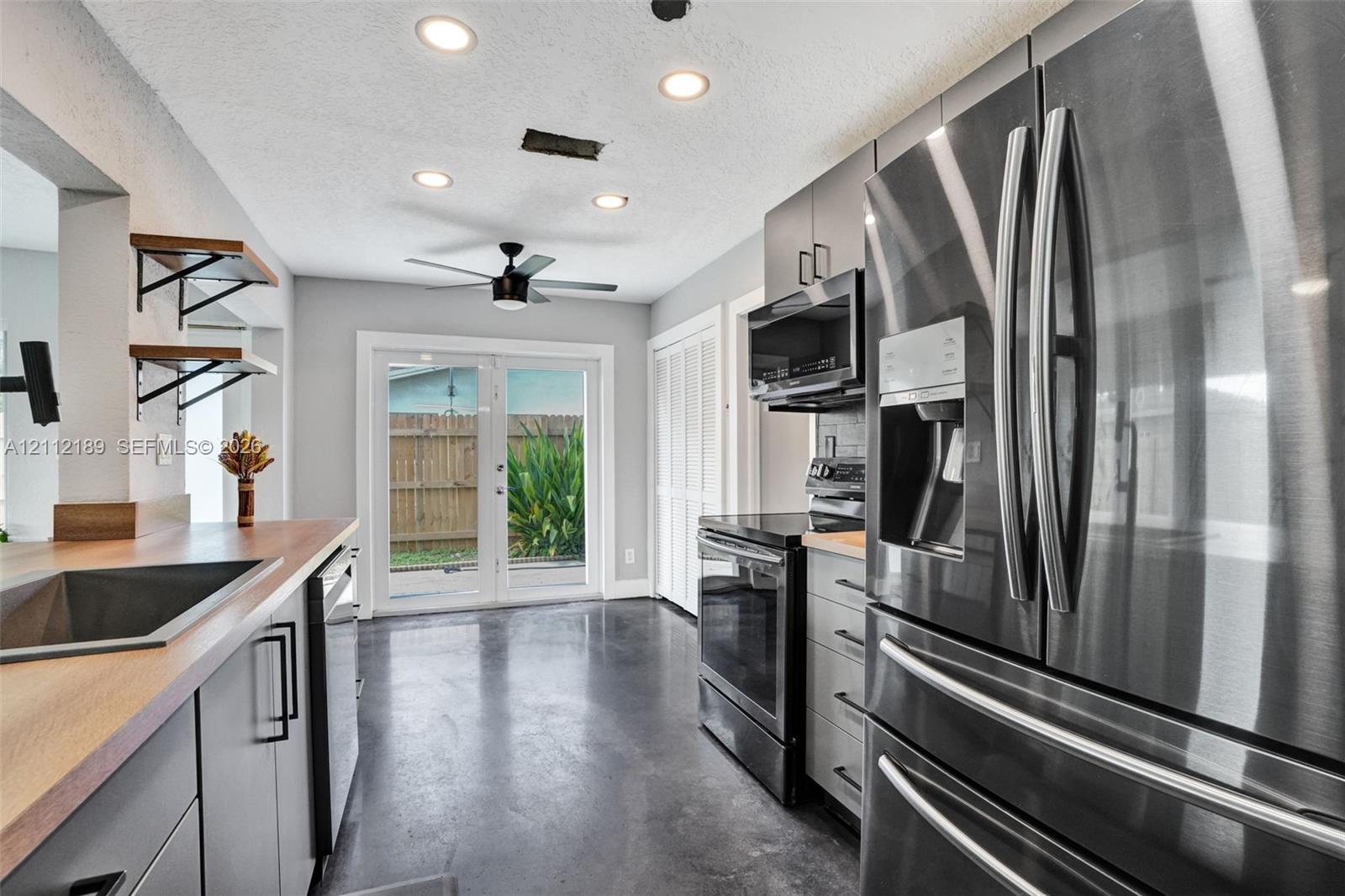 Kitchen featuring stainless steel appliances, wood-finish countertops, recessed lighting, concrete flooring, and glass-paned doors