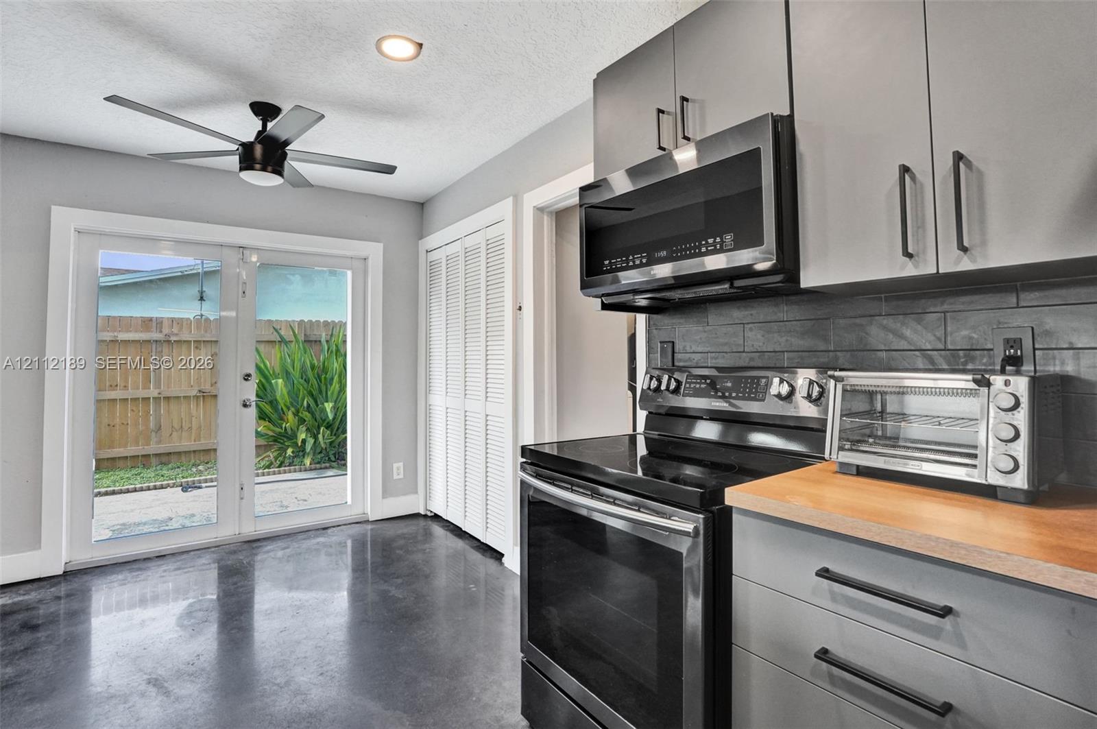 Kitchen featuring grey cabinetry, butcher-block countertops, dark tile backsplash, polished concrete flooring, and double glass-pane doors