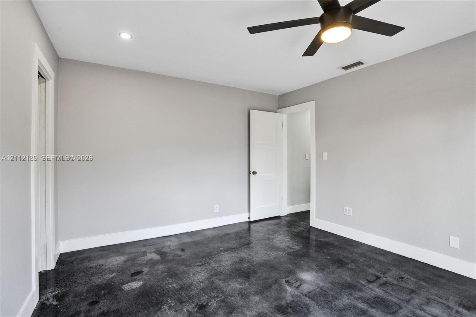 Polished concrete flooring, recessed lighting, matte black ceiling fan with integrated light, and crisp neutral wall paint
