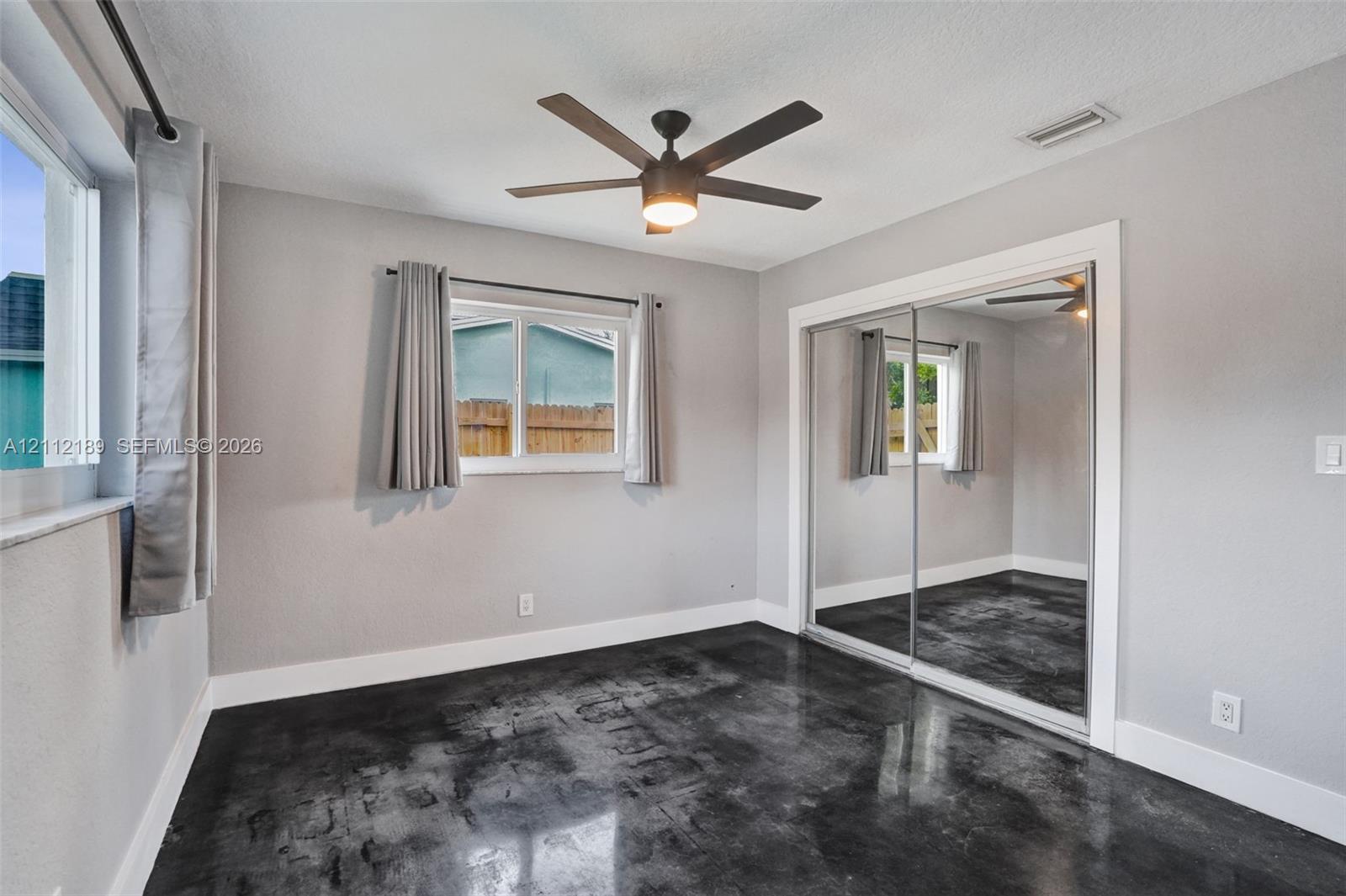 Polished concrete flooring, sliding mirrored closet doors, ceiling fan with integrated lighting, and multi-pane windows