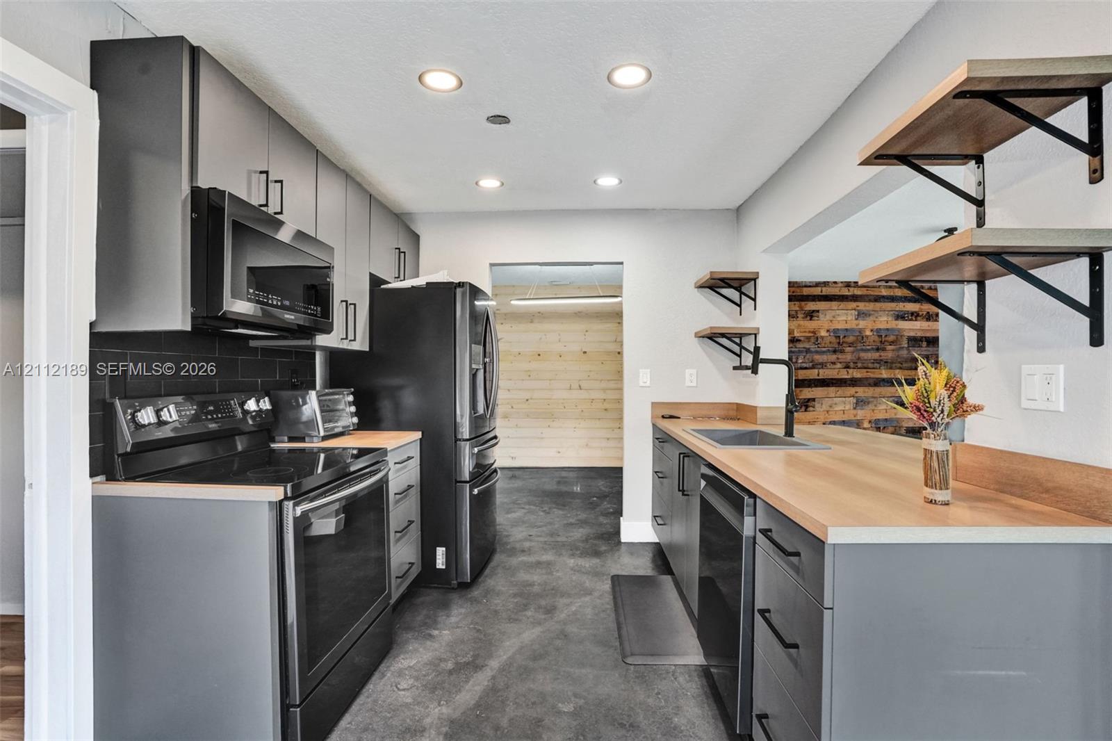 Kitchen featuring matte grey cabinetry, wood-finish countertops, black subway tile backsplash, integrated black appliances, and industrial-style open shelving