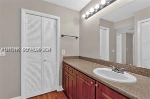 Bathroom featuring a wood-finish vanity with a stone-composite countertop, integrated oval basin, full-width vanity mirror, six-light fixture, and bi-fold louvered closet doors