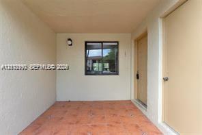 Covered entryway featuring terra-cotta tile flooring, a centered window with dark framing, and a neutral-toned solid door
