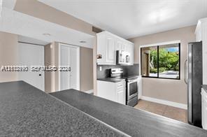 Kitchen featuring a dark-toned laminate countertop peninsula, white shaker-style cabinetry, stainless steel appliances, and tile flooring