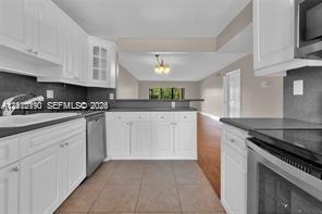 Kitchen featuring white shaker-style cabinetry, dark stone-finish countertops, stainless steel appliances, ceramic tile flooring, and a glass-front display cabinet