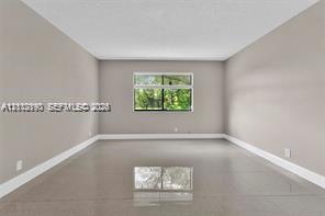 Spacious room featuring neutral paint, large-format tile flooring, and a window with exterior greenery