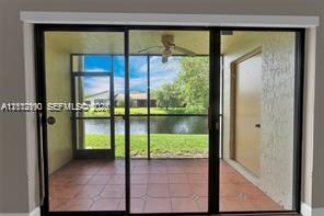 Screened-in lanai featuring tiled flooring, a ceiling fan, and sliding glass door access, opening to a waterfront backdrop