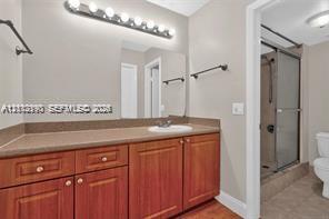 Bathroom featuring a wood-finish vanity with a neutral countertop, recessed sink, integrated multi-bulb vanity lighting, and a glass-enclosed shower