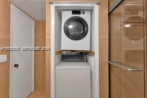 Stacked laundry unit housed in a recessed cabinet with tile surround, featuring glass-enclosed shower stall and panel door