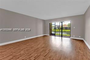 Spacious living area featuring wood-finish flooring, neutral wall paint, and floor-to-ceiling glass sliding doors opening to a screened enclosure Spacious living area featuring wood-finish flooring, neutral wall paint, and floor-to-ceiling glass sliding doors opening to a screened enclosure
