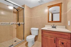 Bathroom featuring a wood-tone vanity cabinet, stone-surfaced countertop, integrated sink, walk-in glass-enclosed shower, and wall-mounted wooden mirror frame