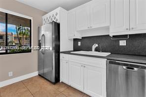 Kitchen featuring white shaker-style cabinetry, stainless steel appliances, a dark solid-surface countertop, an integrated wine rack, and tile flooring Kitchen featuring white shaker-style cabinetry, stainless steel appliances, a dark solid-surface countertop, an integrated wine rack, and tile flooring