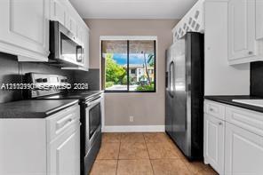 Kitchen featuring white shaker-style cabinetry, dark stone-finish countertops, stainless steel appliances, a built-in wine rack, and tile flooring Kitchen featuring white shaker-style cabinetry, dark stone-finish countertops, stainless steel appliances, a built-in wine rack, and tile flooring
