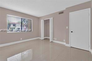 Neutral-toned interior featuring large-format tile flooring, a horizontal sliding window with blinds, and a built-in closet with double doors