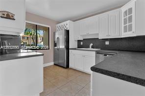 Kitchen featuring white cabinetry with glass-panel display doors, built-in wine storage, stainless steel refrigerator, dark solid-surface countertops, and tiled flooring