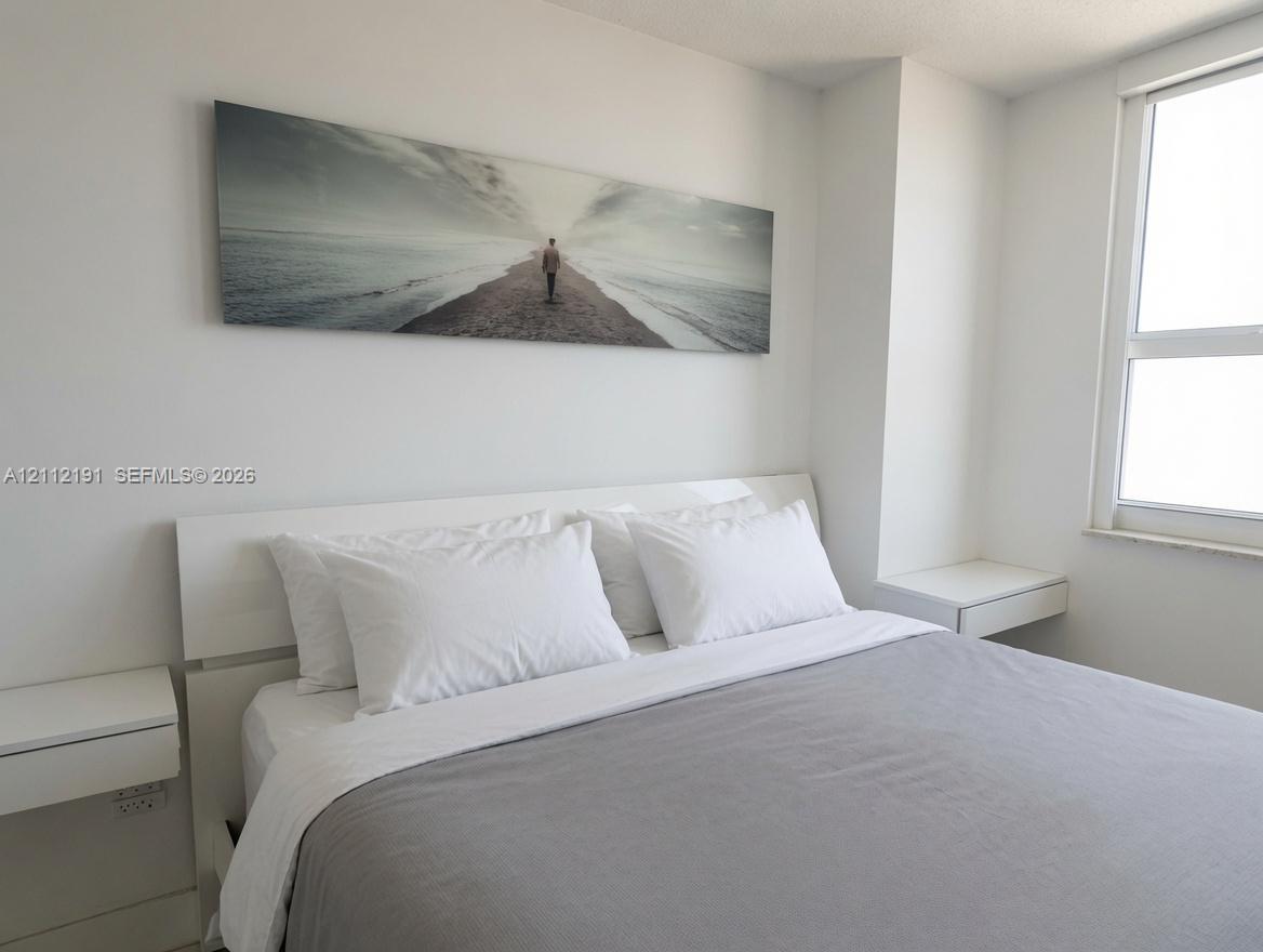 Neutral-toned interior featuring smooth wall finishes, a large multi-pane window, and dual wall-mounted floating bedside surfaces