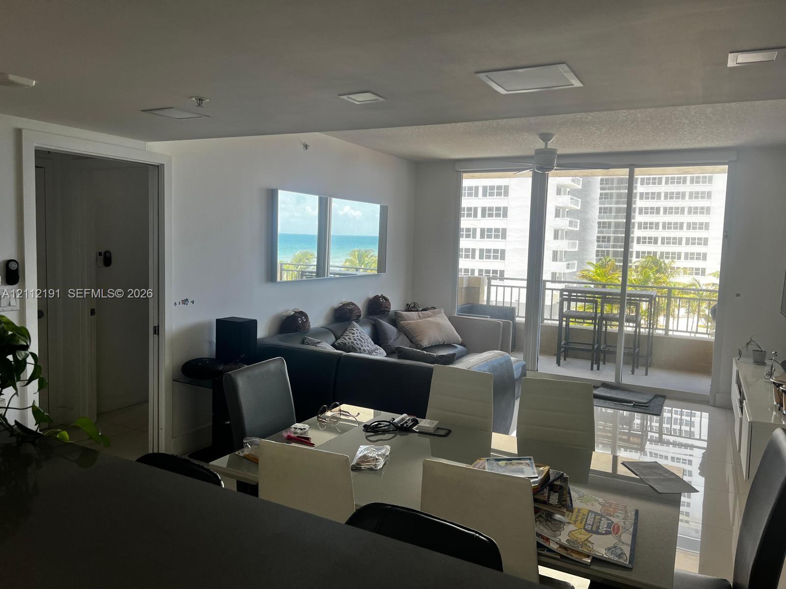 Open-concept interior featuring recessed ceiling lighting, large-format tile flooring, a balcony with a metal railing, and floor-to-ceiling glass sliding doors