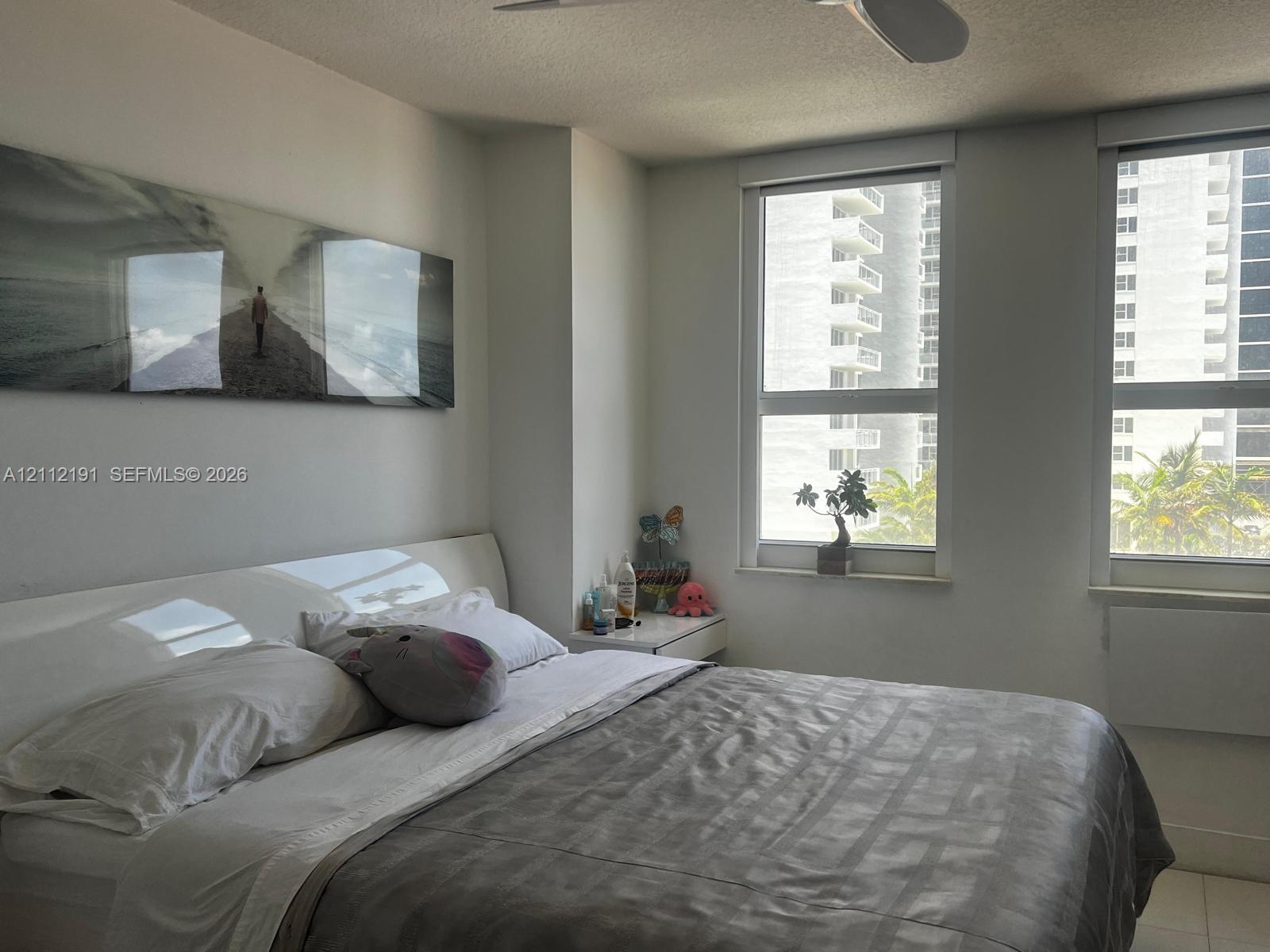 Neutral-toned interior featuring dual oversized windows, light-colored tile flooring, and a white ceiling-mounted fan